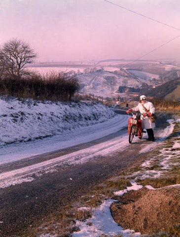 A postwoman pushes her motorcycle up a hill in snow
