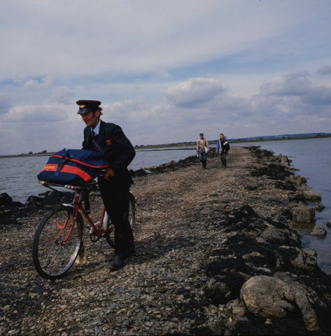 Postman Ken Chaplin pushing his bicycle across a causeway